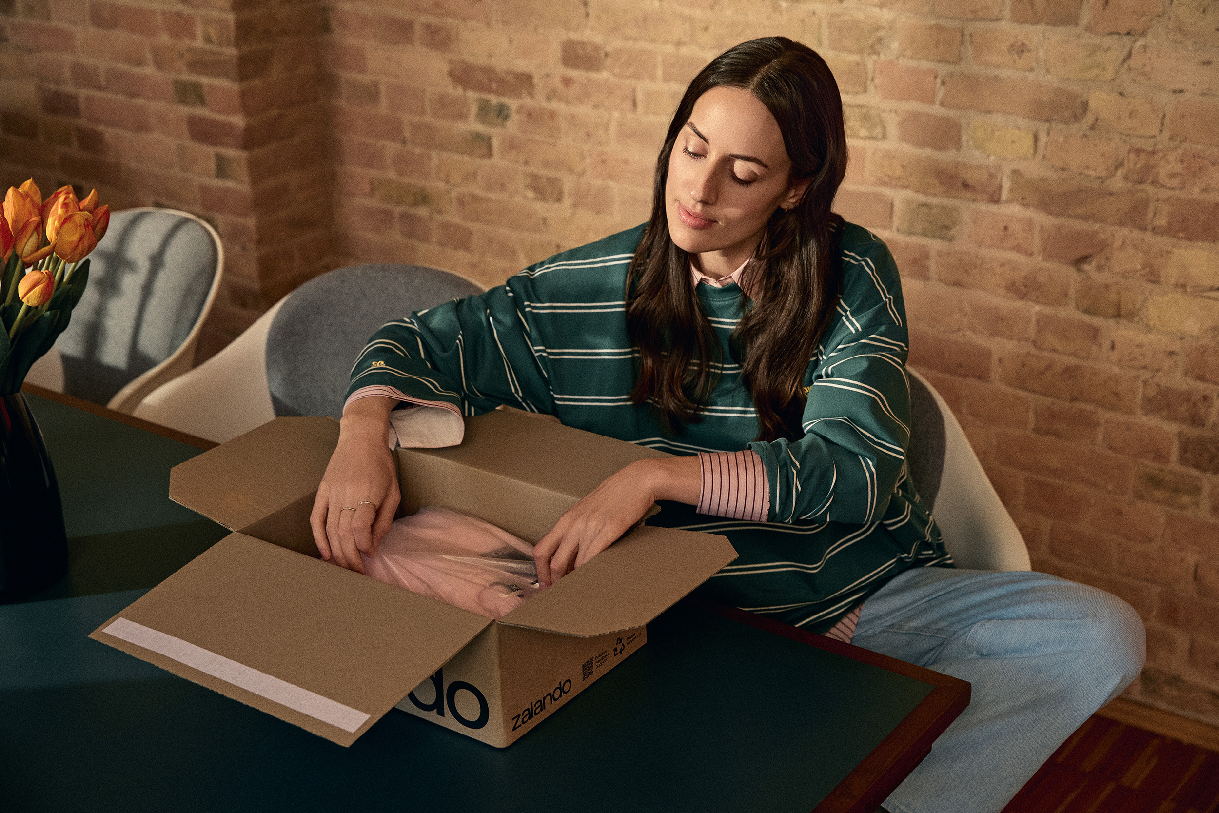 A woman sitting comfortably at a table unpacking a Zalando parcel