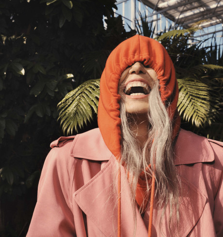 Laughing fashion model with an orange hoodie pulled over her eyes