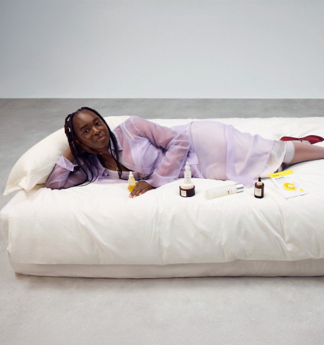 Sophie Carbonari lounging on a big white bed, displaying a variety of beauty products