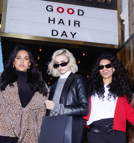 Three models posing for the camera underneath a sign reading: Good Hair Day
