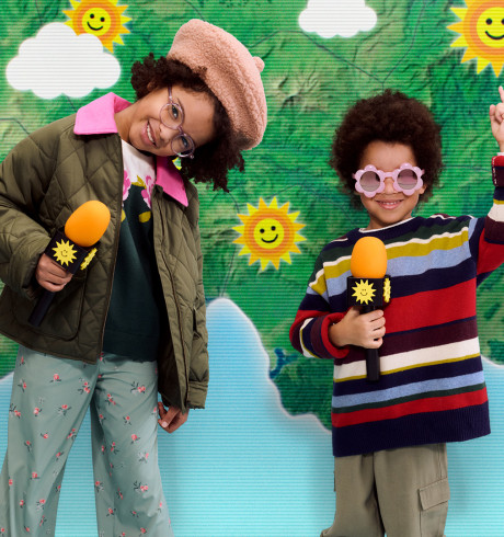 Two kids in playful clothes and microphones posing in front of a childrens' weather map showing only sunshine