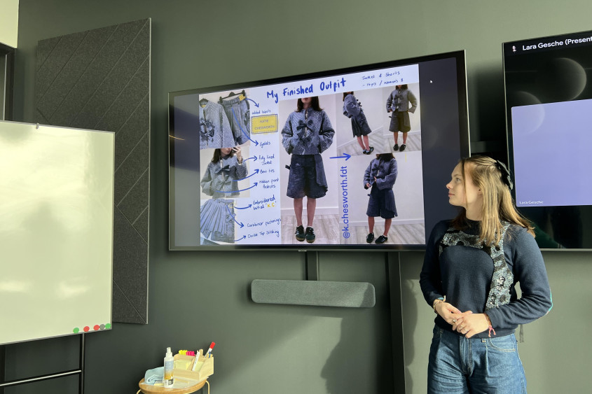 Young female student stands next to a screen where she presents her fashion creations