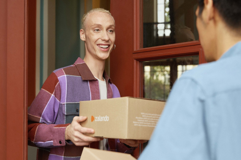 A person receives a Zalando package from a messenger at the front door.