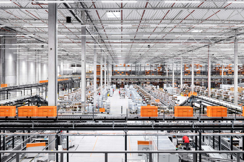 View into a Zalando fulfillment center. A large hall with workstations and numerous conveyor belts with big orange boxes