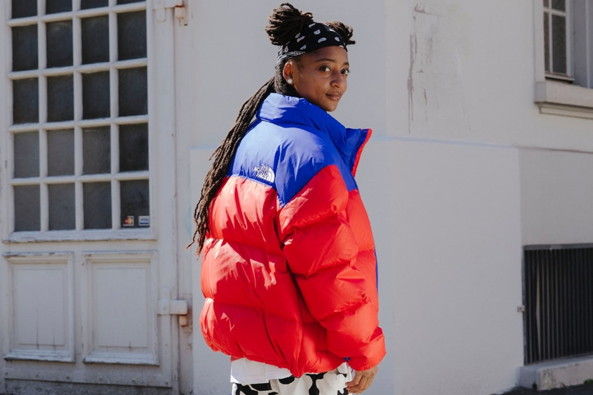 KT Gorique wearing a bright red and blue jacket in front of a white house