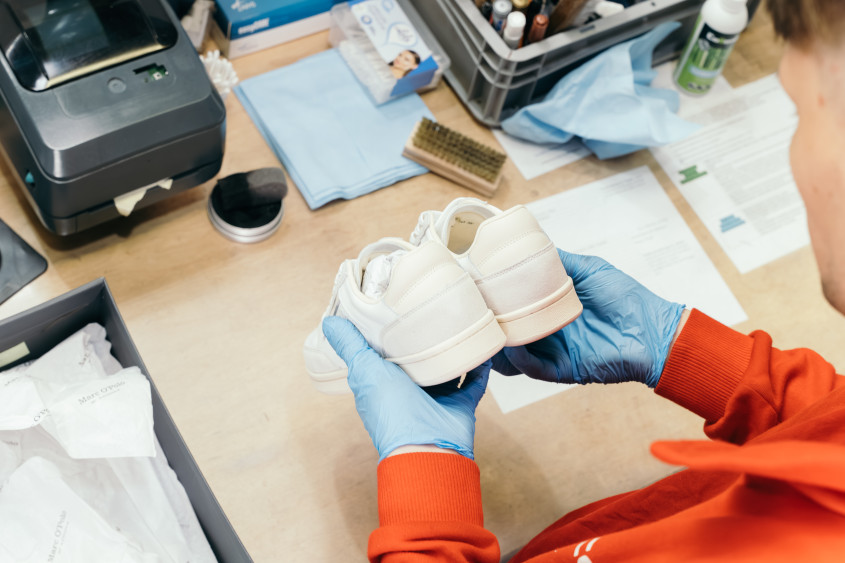 A pair of sneakers is being checked by a person wearing blue protective gloves