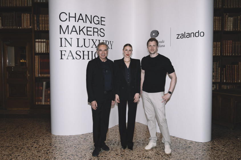 Carlo Capasa, Lena-Sophie Roeper, David Schneider in formal wear posing in front of a photo backdrop with their respective logos
