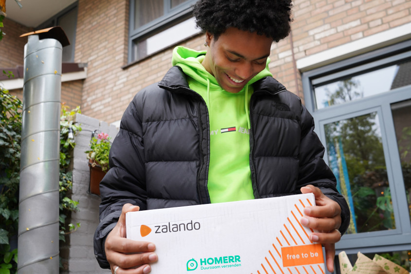 Man walking in the street with a Zalando- and Homerr-branded parcel