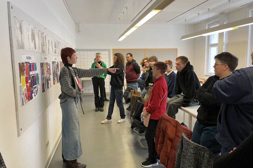 Group of students and athletes standing in a classroom setting looking at a woman at the front who is pointing her finger at one of them
