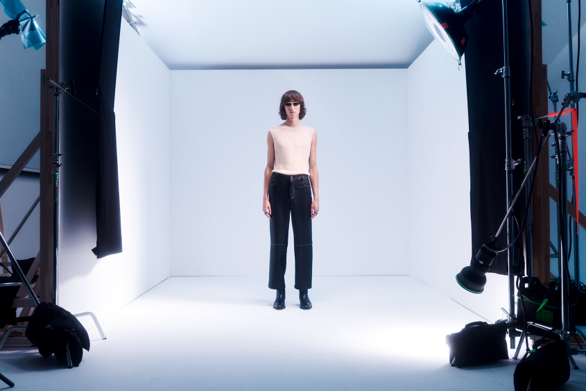 Fashion model on set; white background, camera equipment in the foreground framing them