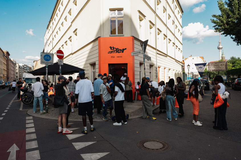 A group of people gathered in front of the building with the bright orange ‘The Corner’ sign over the entrance in Berlin