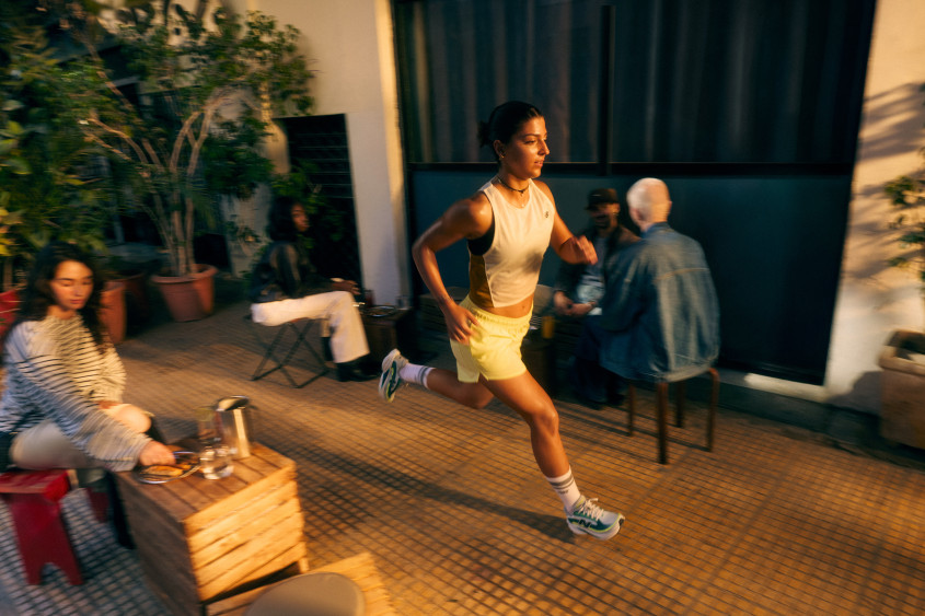 A female athlete running through what looks like an urban sidewalk cafe; warm evening light