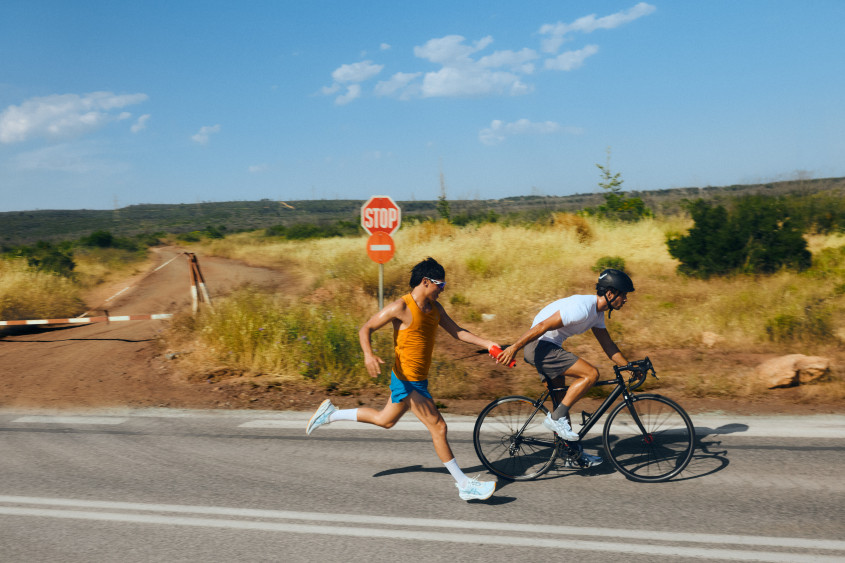 Country road setting, a runner passing a bright red object to a cyclist at full speed