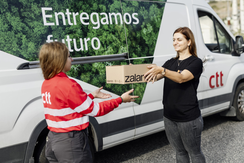A logistics employee handing over a Zalando parcel to the transport partner in a CTT jacket, next to a transport van
