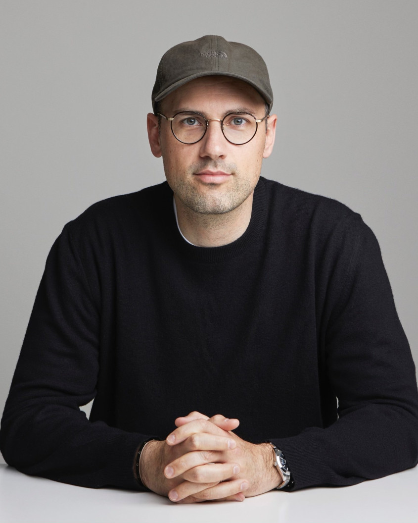 Portrait of David Fischer sitting at a table wearing a black jumper and cap