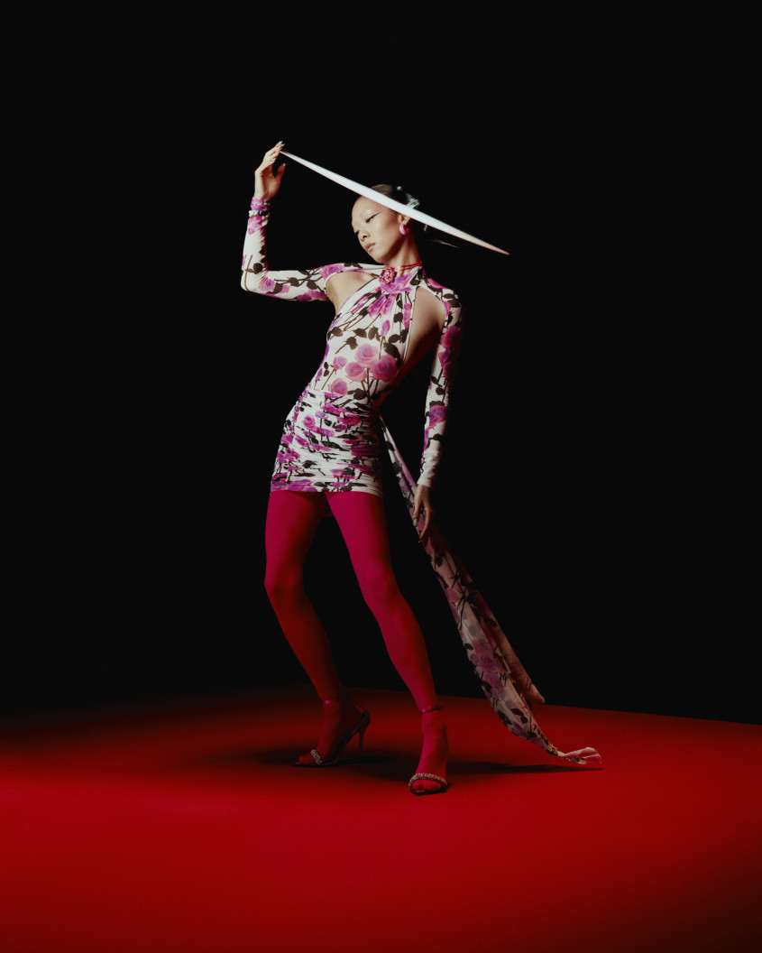 Rina Sawayama standing with a pink dress, red tights and a large hat for Zalando
