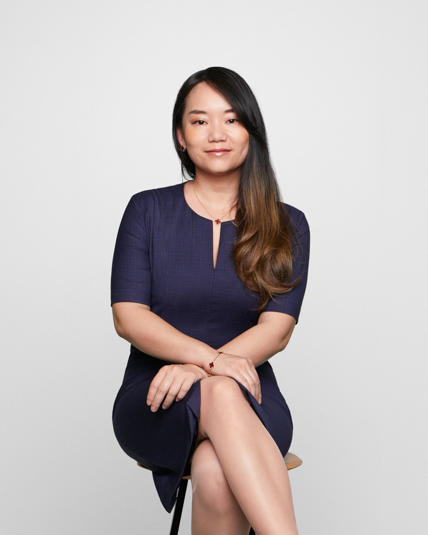 Portrait of Tian Su in a dark blue dress sittting on a chair and looking at the camera