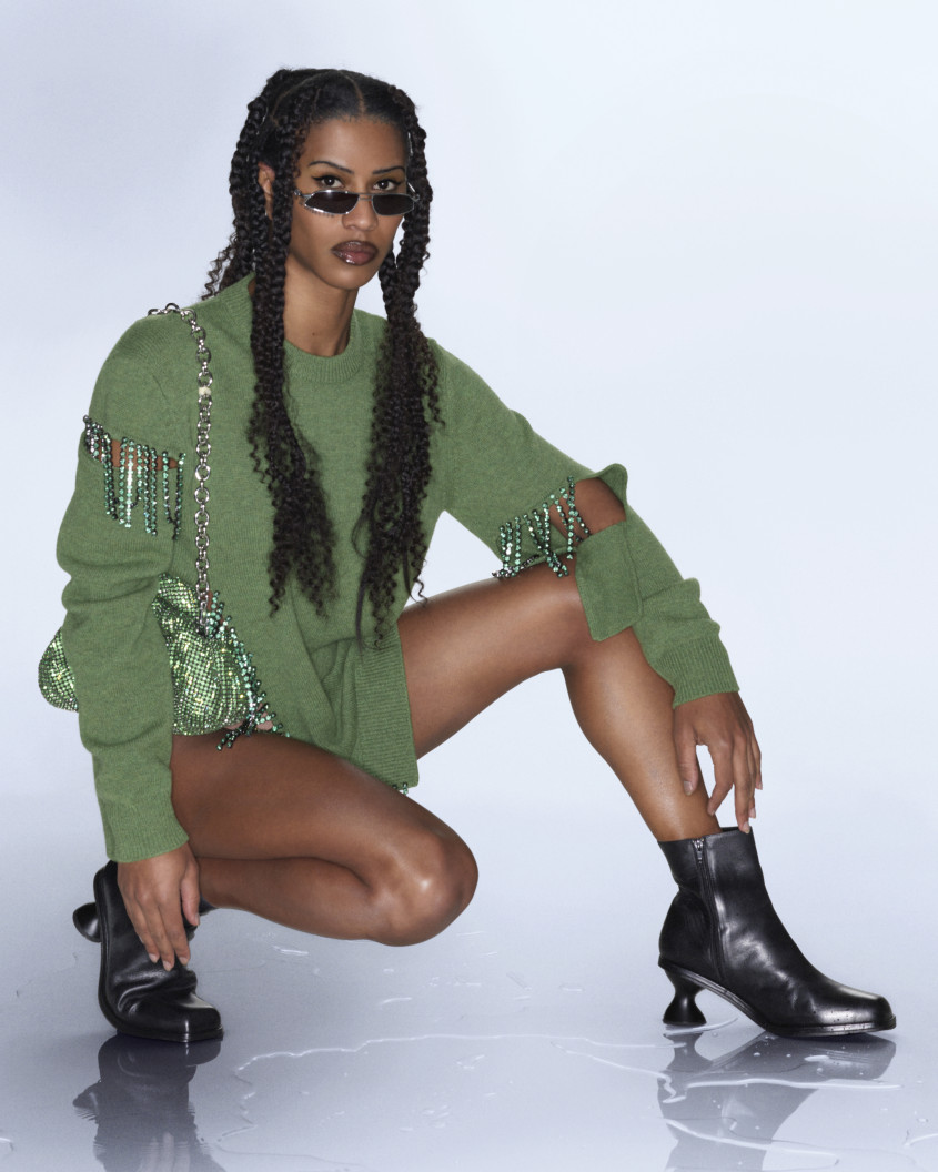 Fashion model wearing sunglasses, a green jumper and black boots.