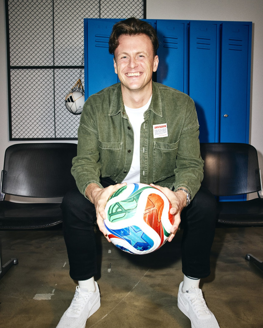 James Rothwell sitting in a locker room setting holding a football and smiling for the camera
