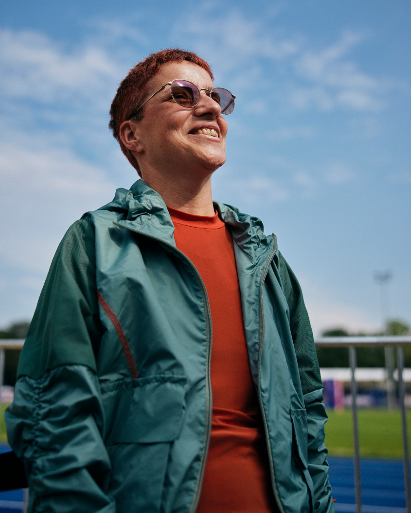 Female athlete wearing sunglasses and casual sportswear looking into the sun; racetrack in the background