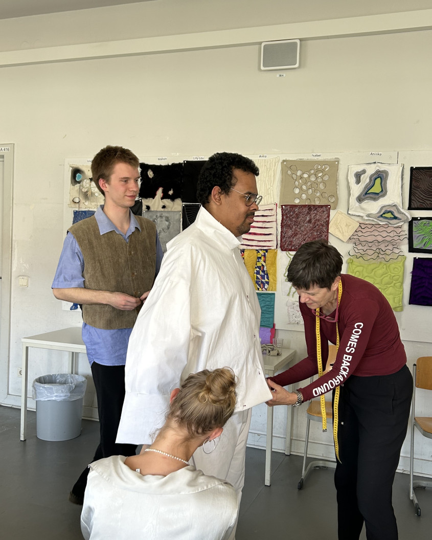 Fitting scenario; male athlete trying on clothes with three designers working on him