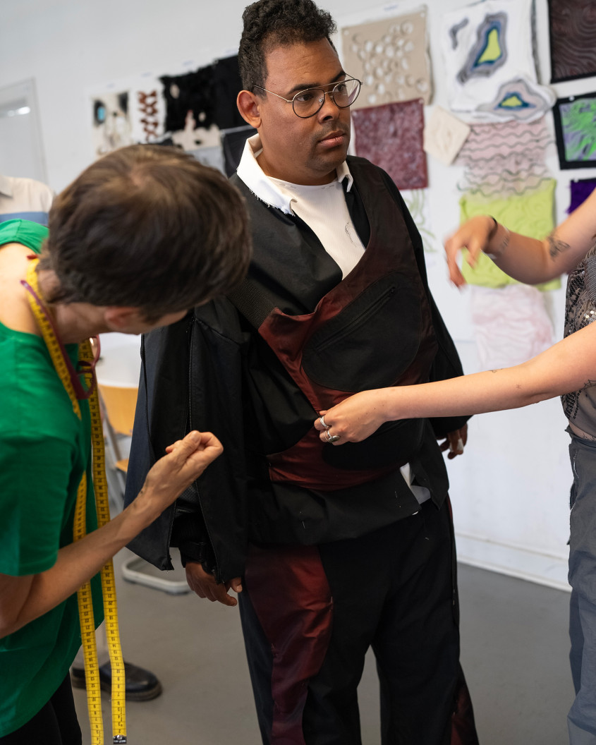 Fitting scenario; male athlete trying on clothes with two designers working on him
