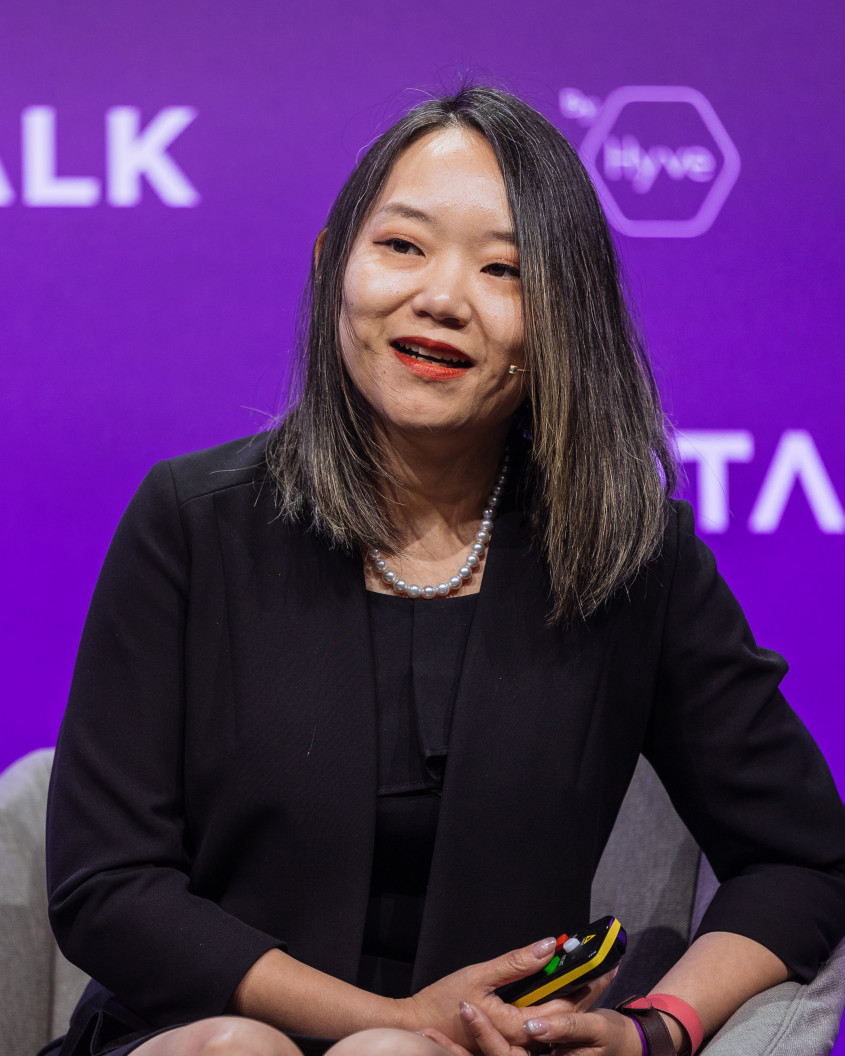 Tian Su talking in front of a purple backdrop with the word Shoptalk