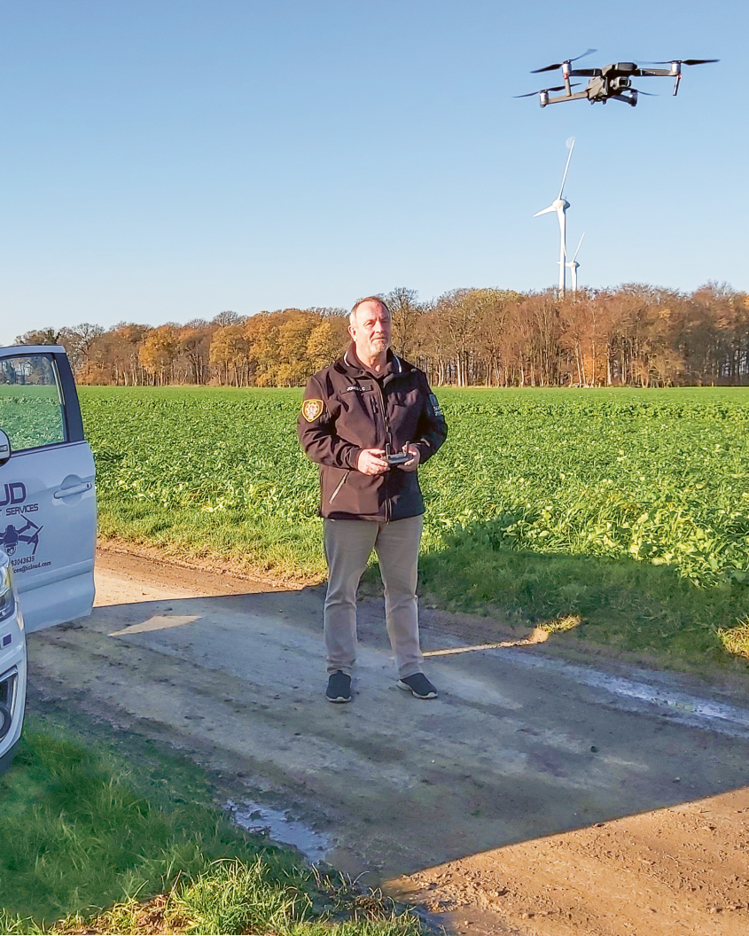 Man steering a drone over an open field; next to him a car with open door