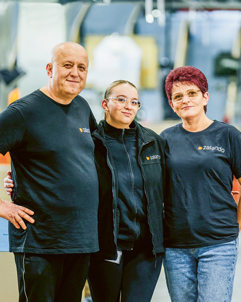 Woman with her parents, all wearing zalando-branded tops, posing for the camera in a warehouse setting