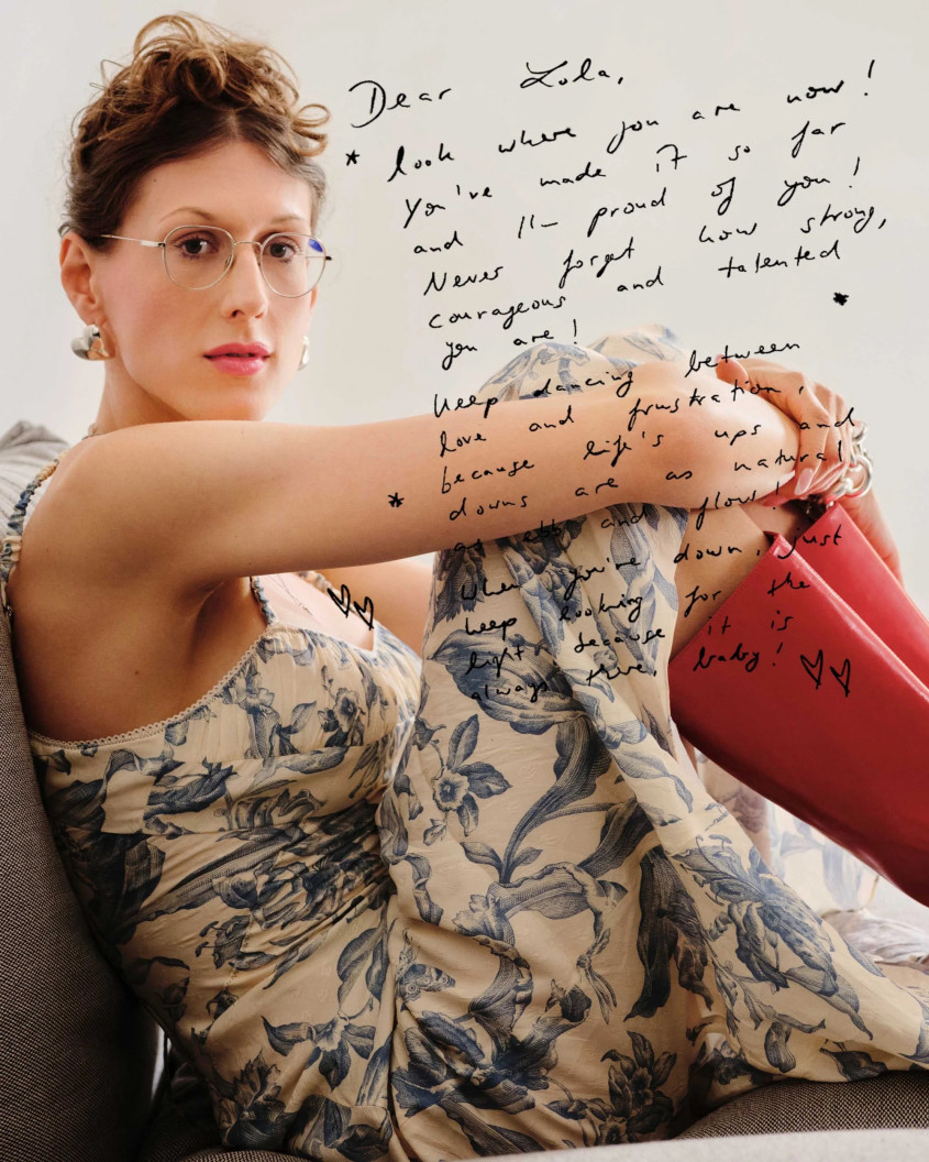 Woman with glasses in a flower dress and red boots, a hand-written text covers part of the picture