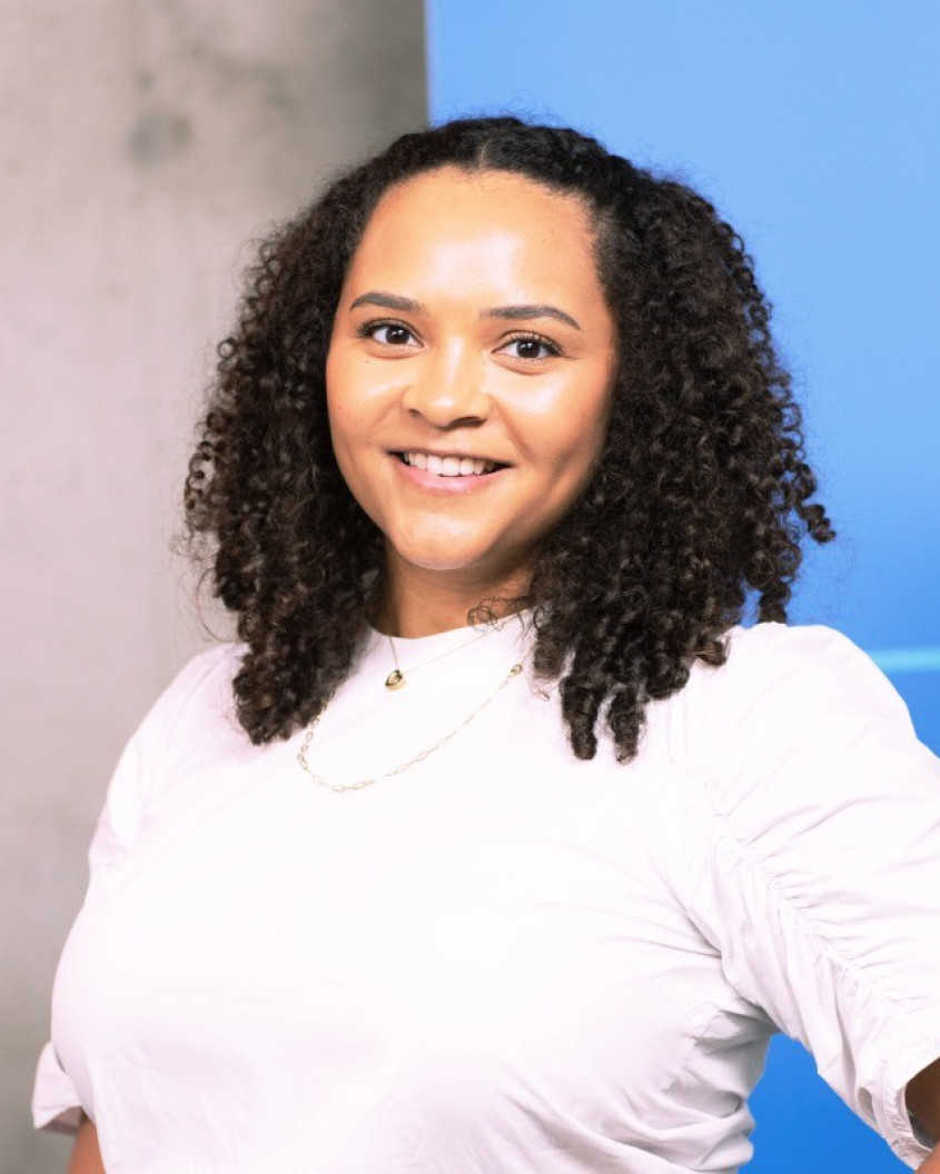 Black woman, wearing a white t-shirt in front of a coloured grey and blue wall