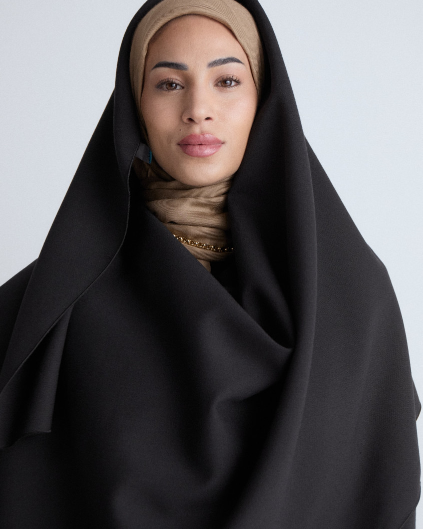 Close up of a model looking straight into the camera with a wide black cape over a brown hijab.