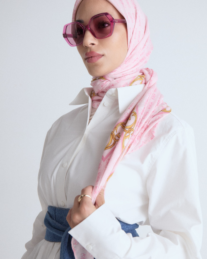 Close up of a model with big pink sunglasses and matching hijab, wearing an oversized formal white shirt and a jeans belt.