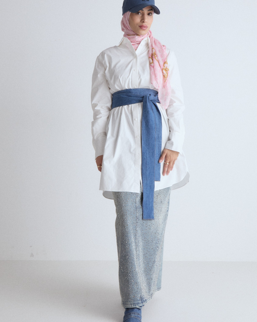 Full body picture of a model, wearing an oversized formal white shirt on top of a long glitter skirt, combined with big pink sunglasses, pink hijab and jeans cap, jeans belt and jeans shoes.