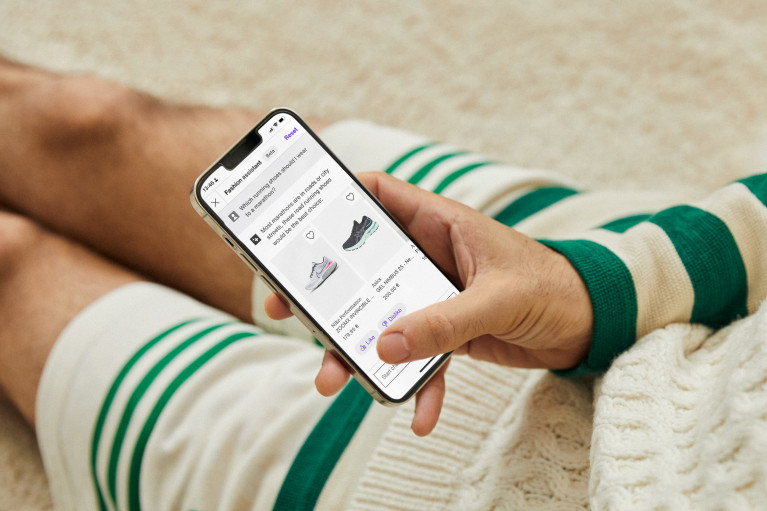 A Zalando customer sitting on the floor looking at the Zalando fashiobn assistant on his mobile phone; only hand and part of their legs are visible