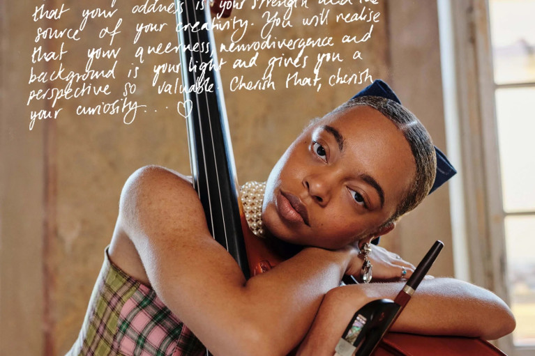 a Black woman hugging a double base in a patterned top, with a hand-written text covering part of the photo