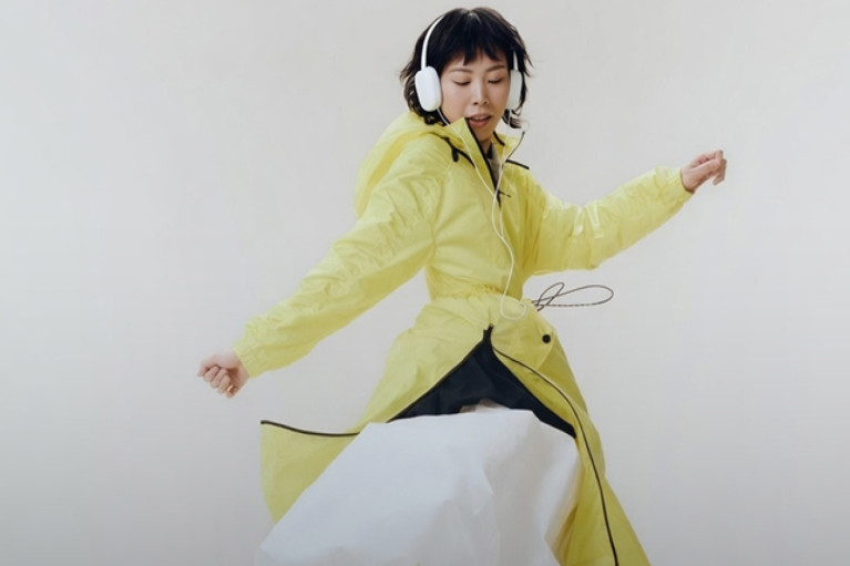 A female model dancing with over-ear headphones and wearing a bright yellow raincoat