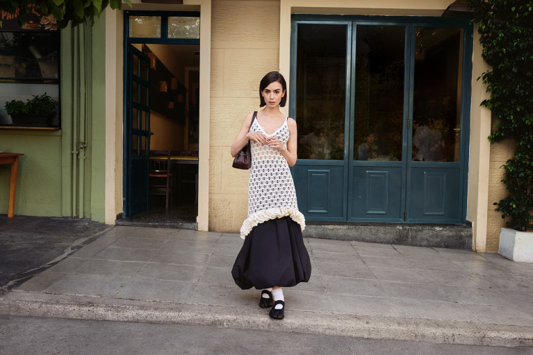 Lily Collins posing in front of what looks like a quaint little café