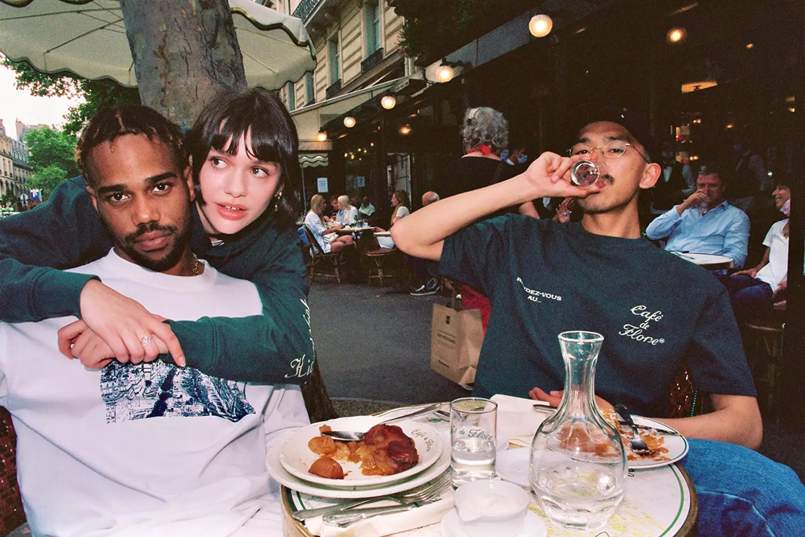 Three young people at a busy sidewalk cafe table with a half eaten meal in front of them