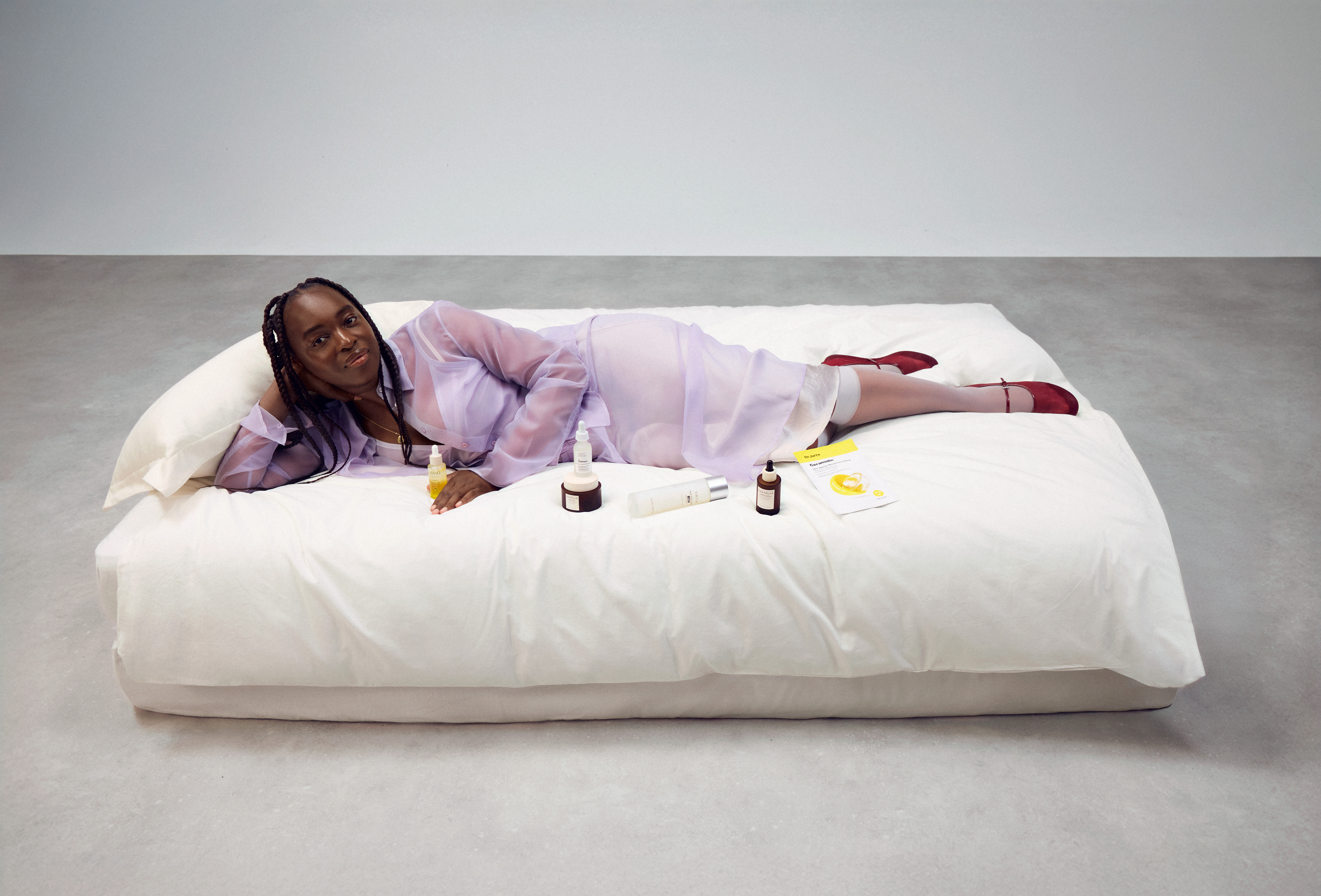 Sophie Carbonari lounging on a big white bed, displaying a variety of beauty products
