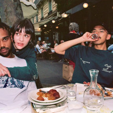 Highsnobiety_Not-in-Paris-Lookbook Three young people at a busy sidewalk cafe table with a half eaten meal in front of them