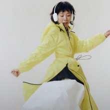 A female model dancing with over-ear headphones and wearing a bright yellow raincoat