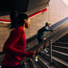 Two runners speeding up the stairs from what looks like a subway station, from the dark out towards the light