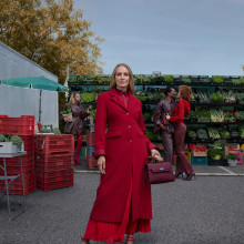 Uma Thurman stands in a red coat at a marketplace for our Autumn Winter campaign 2025