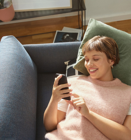 Female customer lying on a sofa, smiling at her phone