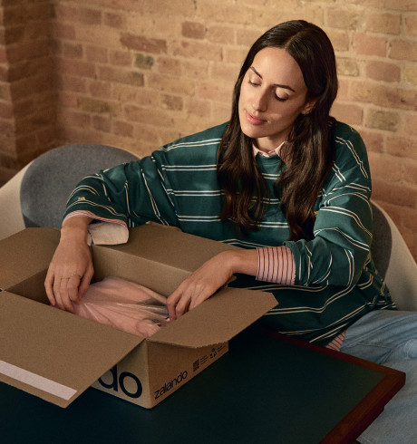 A woman sitting comfortably at a table unpacking a Zalando parcel