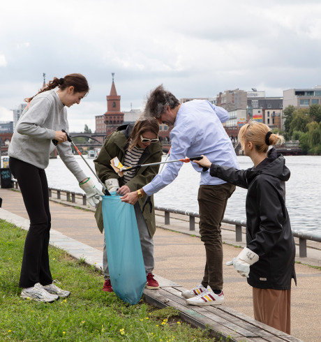 A group of volunteers collecting garbage at Berlin's East side gallery park; Oberbaumbrücke and Spree in the background