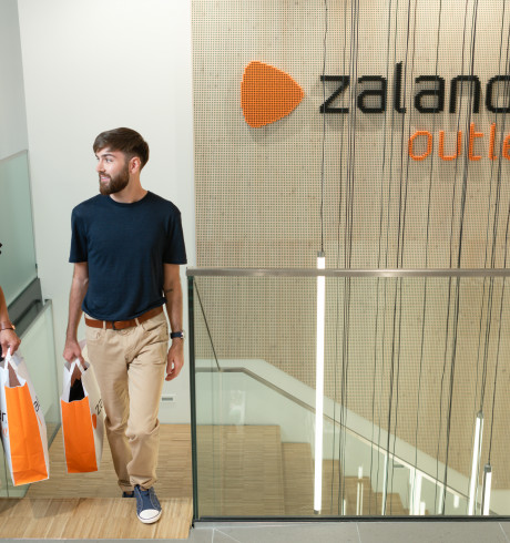 two customers with orange Zalando shopping bags coming up the stairs inside an outlet store