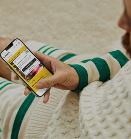 A Zalando customer sitting on the floor looking at the Zalando fashion assistant on his mobile phone; only hand and part of their legs are visible