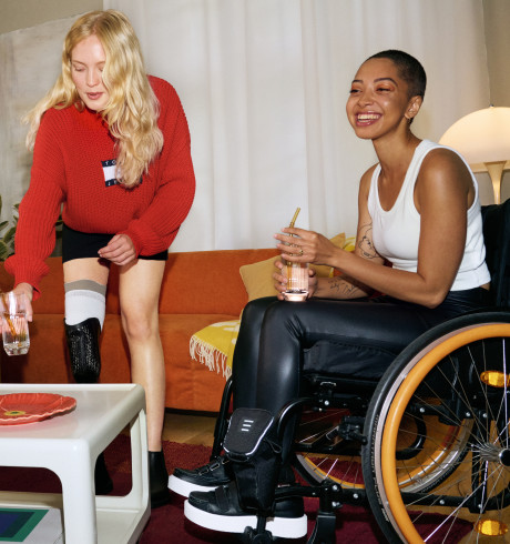 Three interacting young people in a living room scenario; one with a leg brace, one in a wheelchair